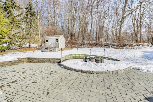 snow covered patio featuring an outdoor fire pit and an outdoor structure