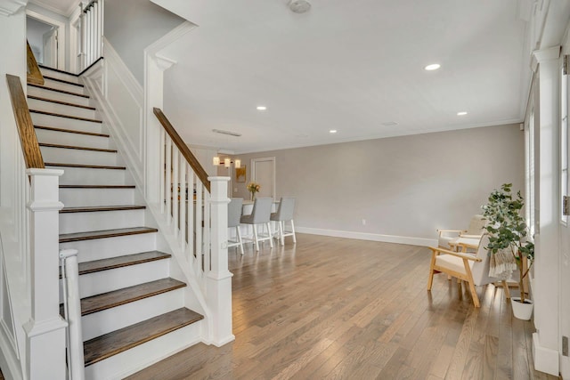 stairs featuring hardwood / wood-style flooring, recessed lighting, baseboards, ornamental molding, and an inviting chandelier