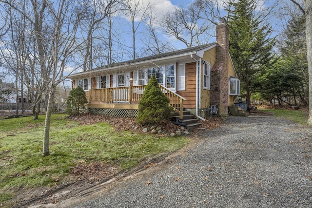 view of front of property with a front lawn, gravel driveway, a chimney, and a wooden deck