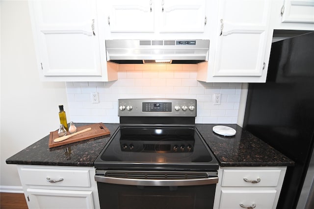 kitchen featuring under cabinet range hood, white cabinets, freestanding refrigerator, stainless steel electric range oven, and dark stone countertops