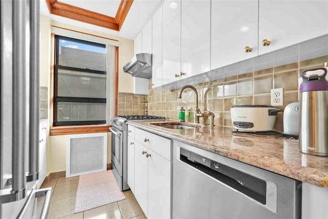 kitchen with wall chimney exhaust hood, appliances with stainless steel finishes, a sink, and white cabinetry