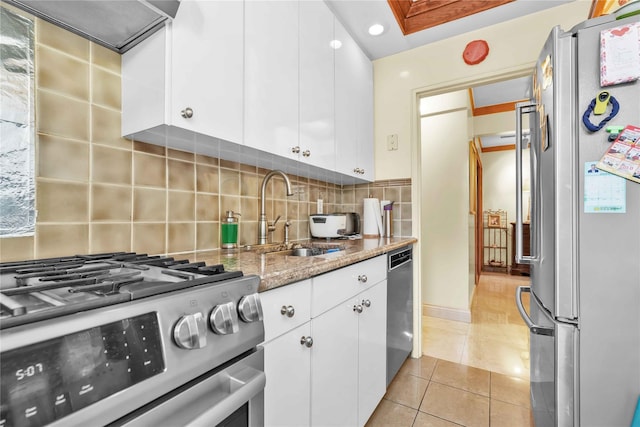 kitchen featuring light stone counters, light tile patterned floors, stainless steel appliances, white cabinetry, and a sink