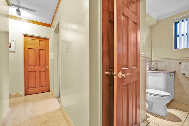 bathroom with crown molding, tile walls, toilet, wainscoting, and a sink