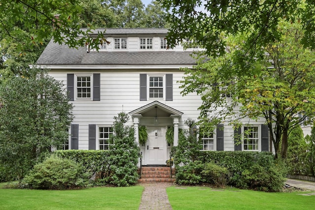 colonial inspired home featuring entry steps, a front lawn, and roof with shingles