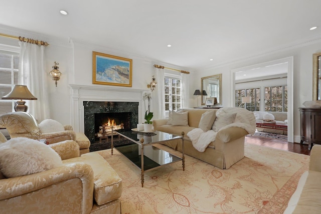 living room featuring ornamental molding, a high end fireplace, light wood-style floors, and plenty of natural light