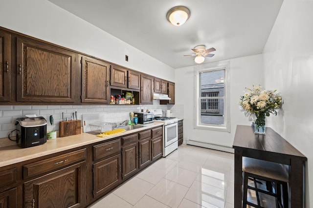 kitchen featuring white range with gas cooktop, a baseboard heating unit, ceiling fan, dark brown cabinets, and tasteful backsplash