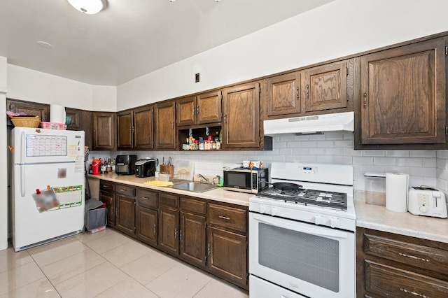 kitchen featuring sink, white appliances, tasteful backsplash, and dark brown cabinetry