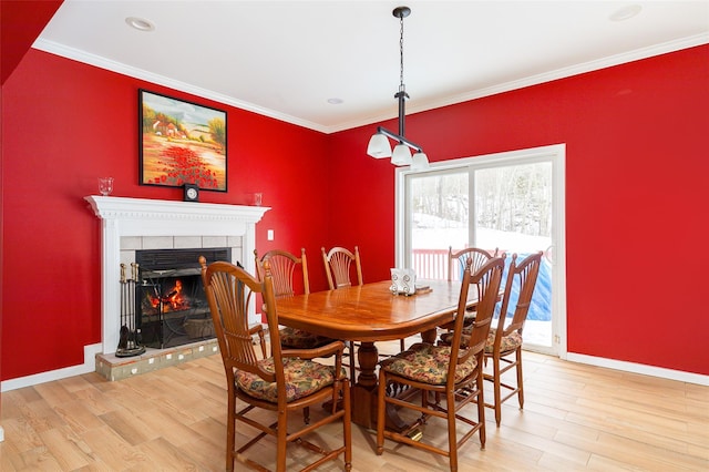 dining room with crown molding, a tile fireplace, and light wood-style flooring