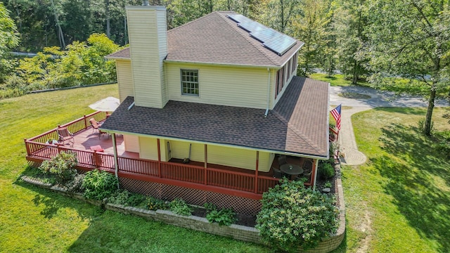 back of property with a yard, a chimney, a deck, and a shingled roof