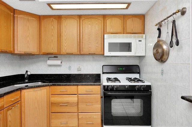 kitchen with white microwave, a sink, brown cabinets, dark stone countertops, and gas range