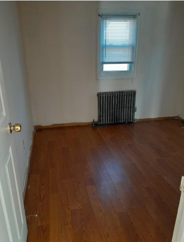 unfurnished room featuring radiator heating unit and hardwood / wood-style flooring