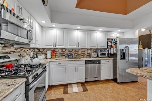 kitchen featuring stainless steel appliances, a raised ceiling, decorative backsplash, white cabinets, and a sink