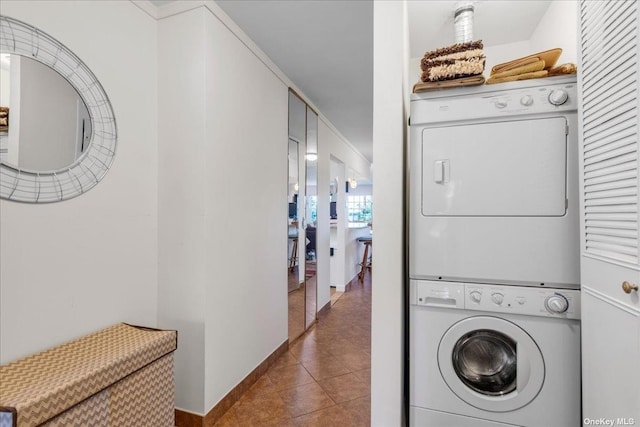 laundry area featuring laundry area, dark tile patterned floors, stacked washer and clothes dryer, and baseboards