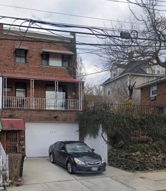 view of front of property with an attached garage, a balcony, concrete driveway, and brick siding