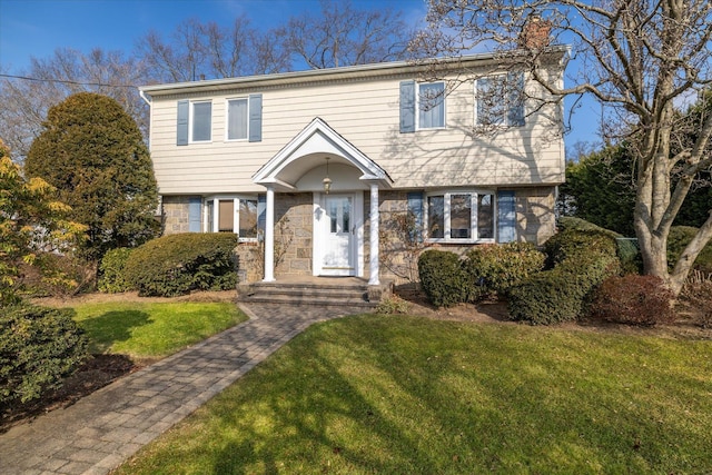 colonial house featuring a front yard, stone siding, and a chimney