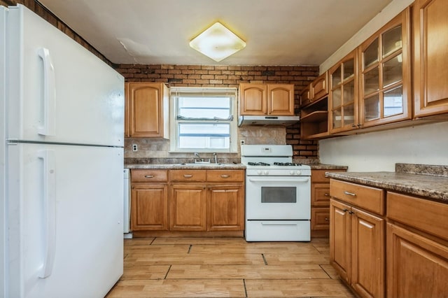 kitchen featuring light wood finished floors, glass insert cabinets, a sink, white appliances, and under cabinet range hood