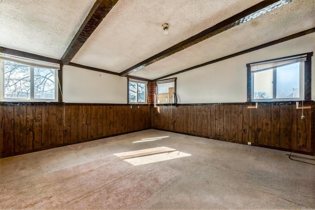 unfurnished room featuring lofted ceiling with beams, carpet floors, a textured ceiling, and wainscoting