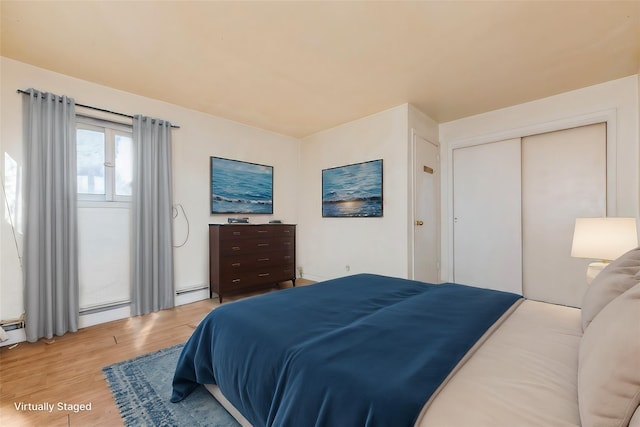 bedroom with a baseboard heating unit, light wood finished floors, and a closet