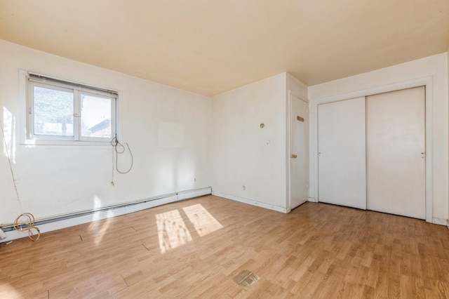 unfurnished bedroom featuring baseboard heating, light wood-type flooring, and a closet