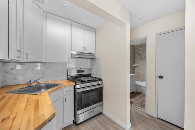 kitchen featuring stainless steel range with gas stovetop, under cabinet range hood, white cabinetry, wooden counters, and a sink