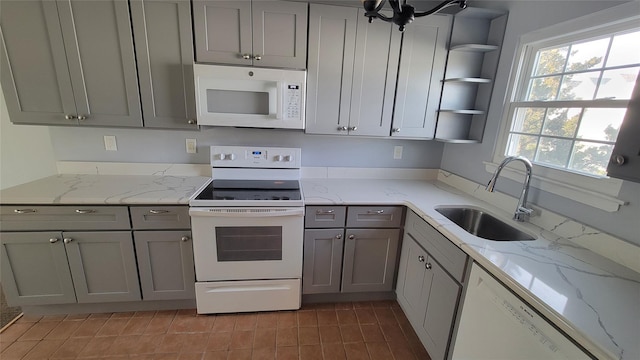 kitchen featuring white appliances, light stone countertops, gray cabinets, open shelves, and a sink