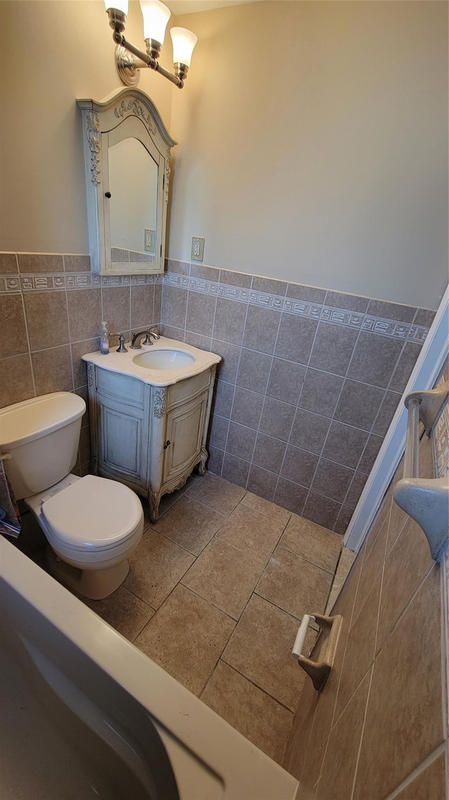 bathroom with tile walls, vanity, toilet, and an inviting chandelier