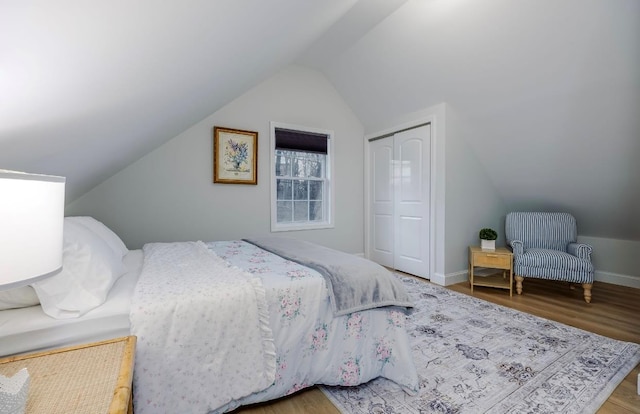 bedroom featuring vaulted ceiling, a closet, wood finished floors, and baseboards