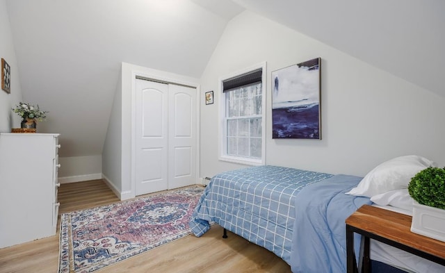 bedroom featuring a closet, a baseboard radiator, lofted ceiling, and light wood-style floors