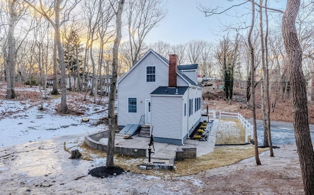 snow covered property with a shingled roof, fence, and a chimney