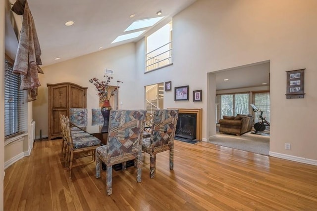 dining room featuring a fireplace with flush hearth, a skylight, light wood-style floors, and high vaulted ceiling