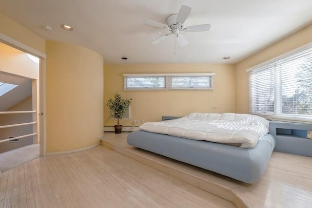 bedroom featuring ceiling fan, multiple windows, a baseboard radiator, and light wood-style floors