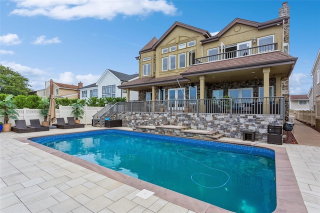 rear view of property featuring a fenced in pool, a patio, stucco siding, fence, and a balcony