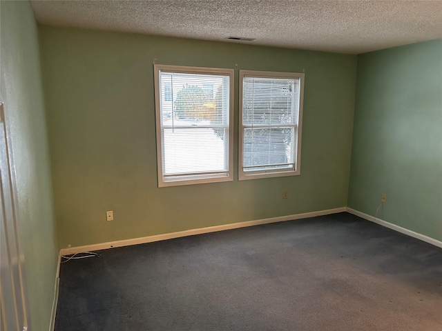 unfurnished room featuring baseboards, visible vents, dark colored carpet, and a textured ceiling