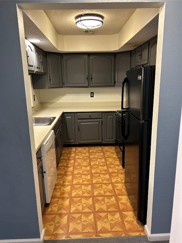 kitchen with a textured ceiling, a sink, light countertops, freestanding refrigerator, and dishwasher