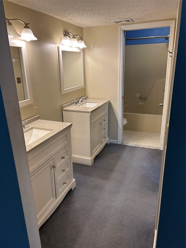 full bathroom featuring visible vents, two vanities, a sink, and a textured ceiling