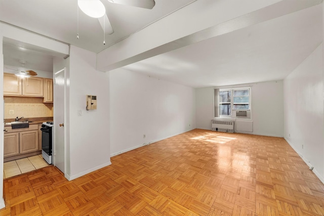 unfurnished living room featuring cooling unit, a sink, a ceiling fan, baseboards, and radiator heating unit