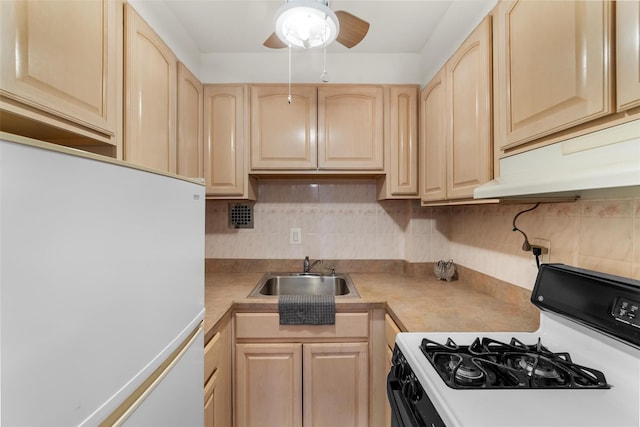 kitchen featuring backsplash, light brown cabinetry, freestanding refrigerator, a sink, and gas range