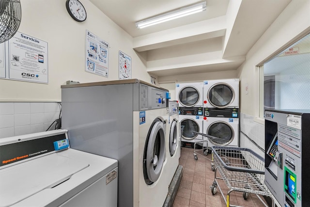 shared laundry area with stacked washer and clothes dryer, a wainscoted wall, tile walls, tile patterned flooring, and washer and dryer