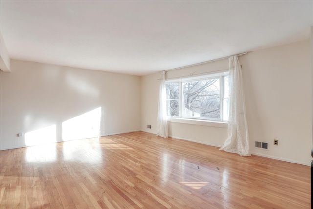 empty room with light wood-style flooring, visible vents, and baseboards