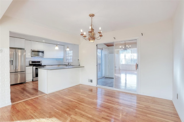 kitchen featuring white cabinets, appliances with stainless steel finishes, a peninsula, hanging light fixtures, and a chandelier