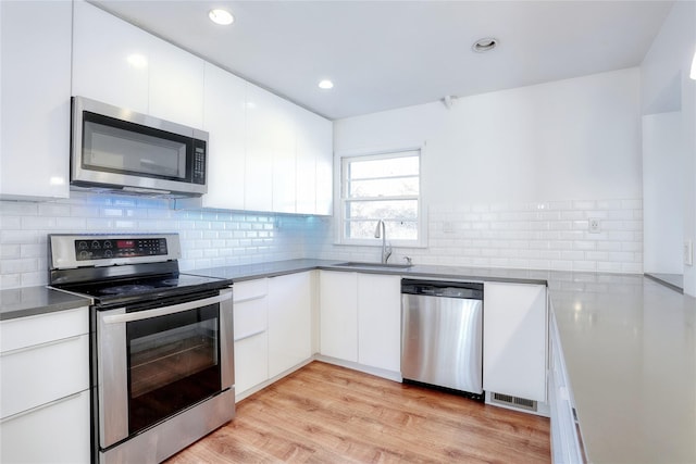 kitchen with stainless steel appliances, a sink, white cabinets, decorative backsplash, and dark countertops