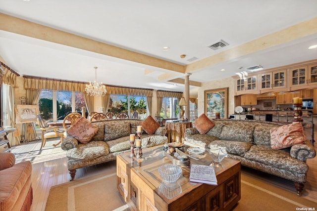 living area featuring beam ceiling, visible vents, light wood-style floors, a chandelier, and ornate columns