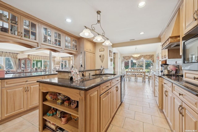 kitchen with pendant lighting, a center island with sink, glass insert cabinets, appliances with stainless steel finishes, and dark stone counters