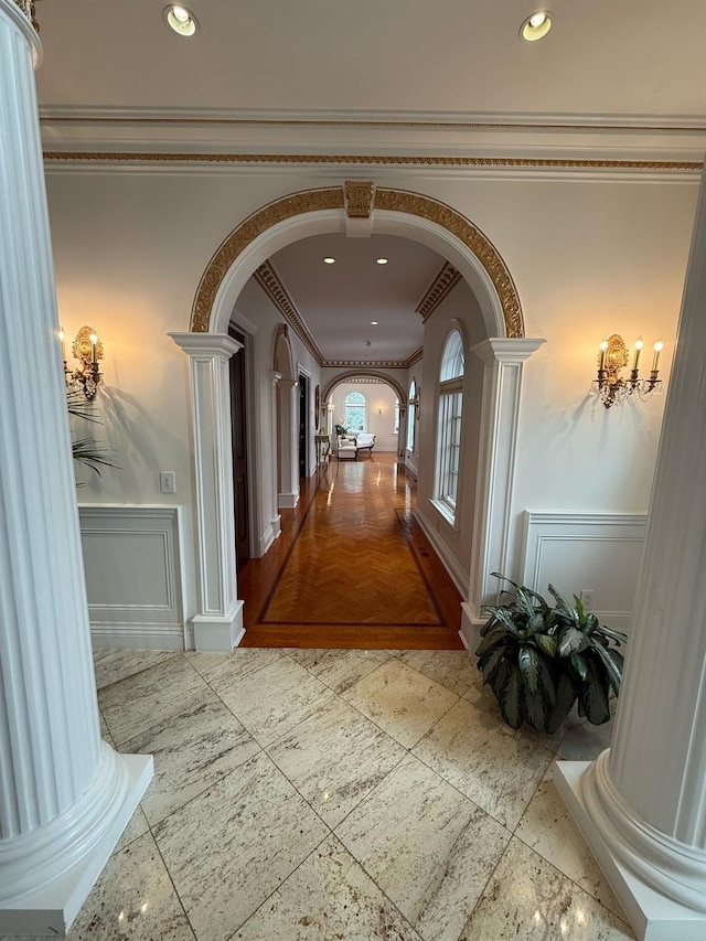 hallway featuring arched walkways, recessed lighting, a decorative wall, ornamental molding, and wainscoting