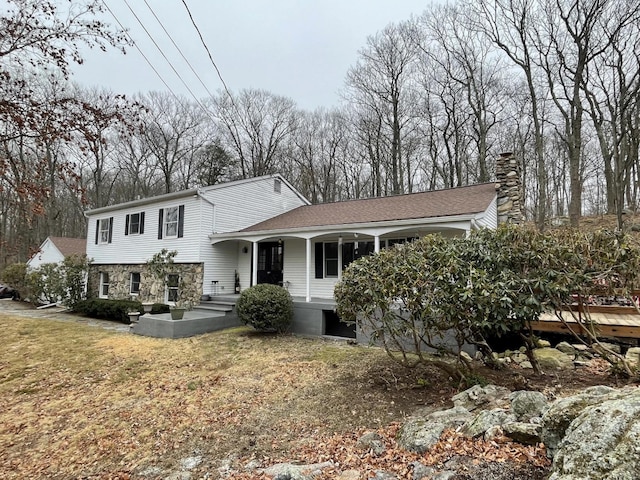 split level home with a chimney, a front yard, and roof with shingles