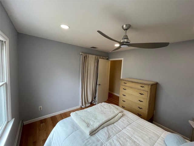 bedroom with visible vents, baseboards, baseboard heating, wood finished floors, and a ceiling fan