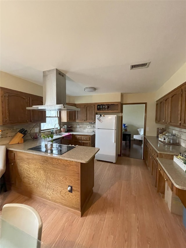 kitchen with tasteful backsplash, black electric stovetop, a peninsula, island exhaust hood, and freestanding refrigerator