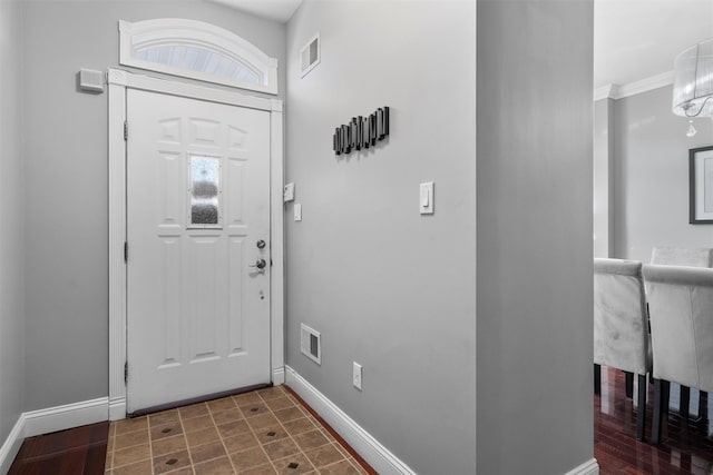 foyer entrance with baseboards, visible vents, and crown molding