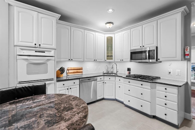 kitchen featuring decorative backsplash, dark stone counters, stainless steel appliances, white cabinetry, and a sink