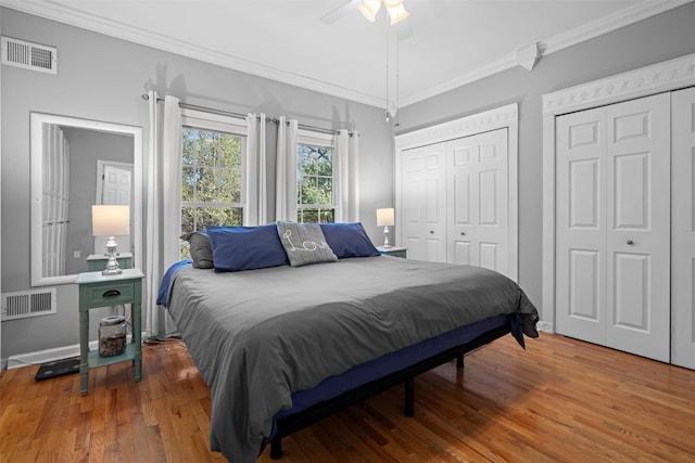 bedroom with multiple closets, wood finished floors, visible vents, and crown molding